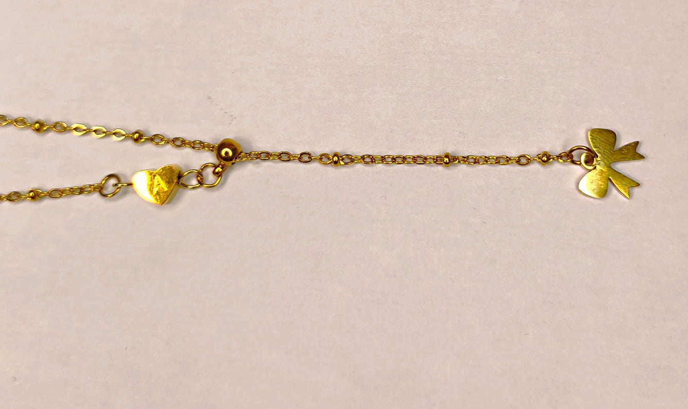 Détail d'un collier doré Y avec petit cœur et un petit nœud doré en bas - Rêve de Rose
