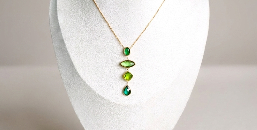 Détail collier Verdia – pendentif trio de cristaux verts sur chaîne dorée en acier inoxydable, présenté sur un buste blanc