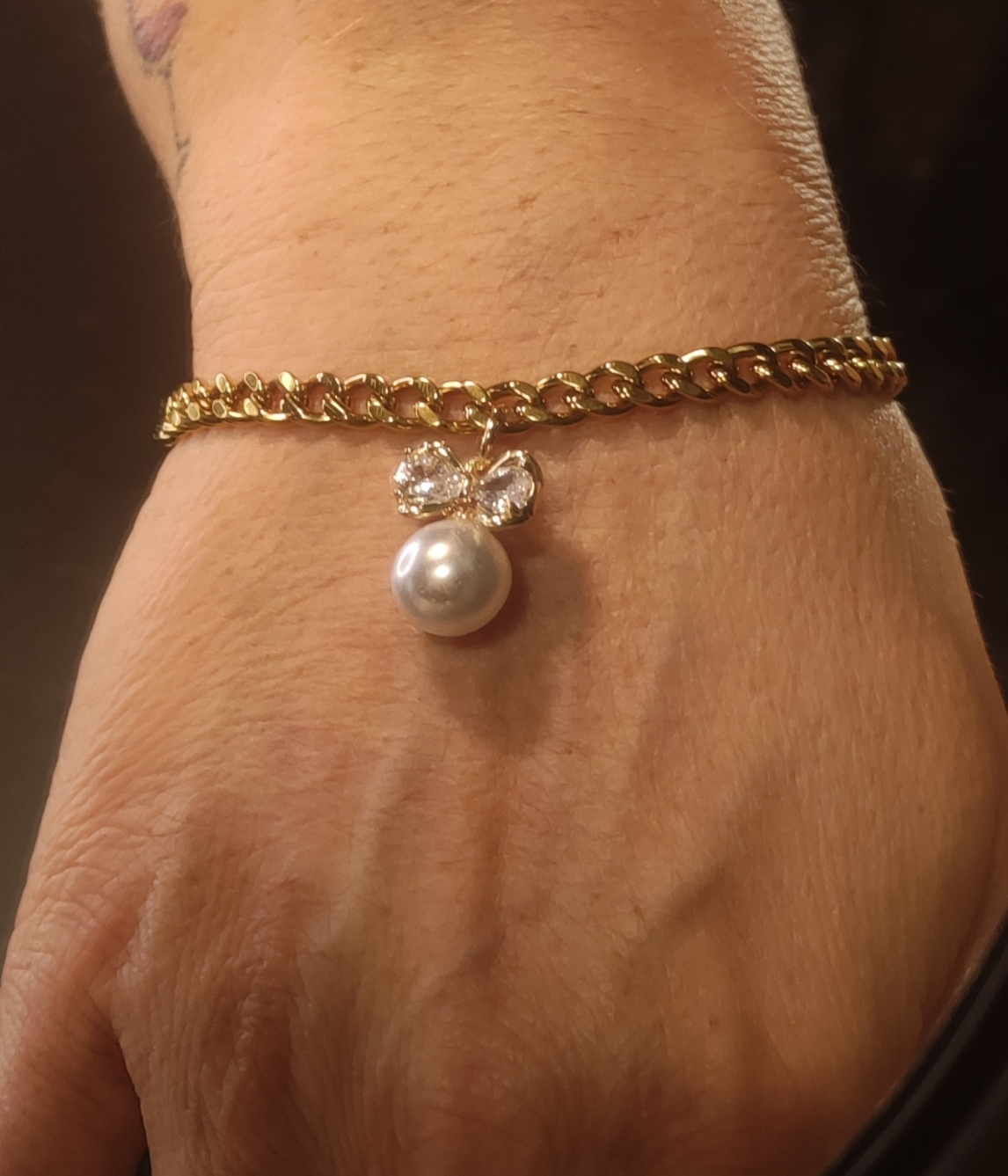 Femme portant un bracelet au maillons serrés avec pendentif nœud et perle blanche - Rêve de Rose