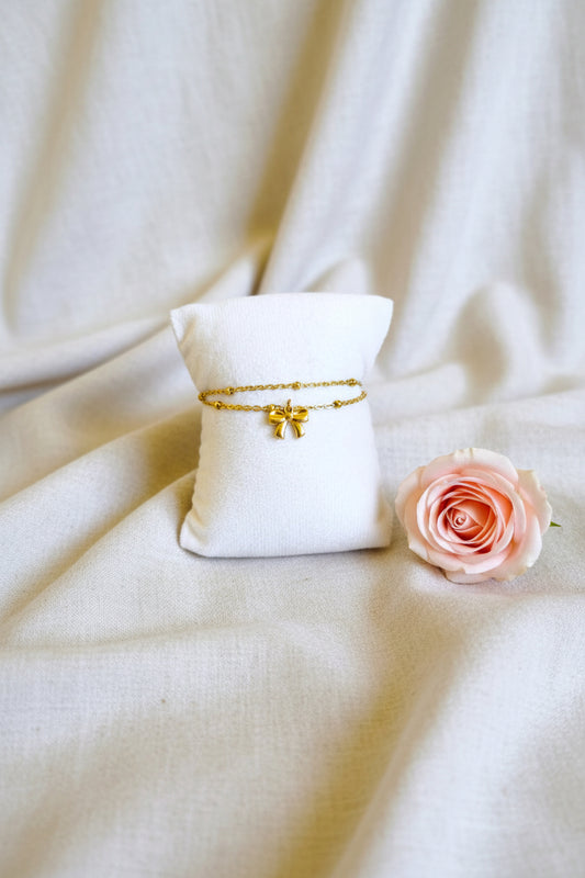 Bracelet double chaîne perles dorées et charm nœud en acier inoxydable doré, présenté sur coussin - Rêve de Rose