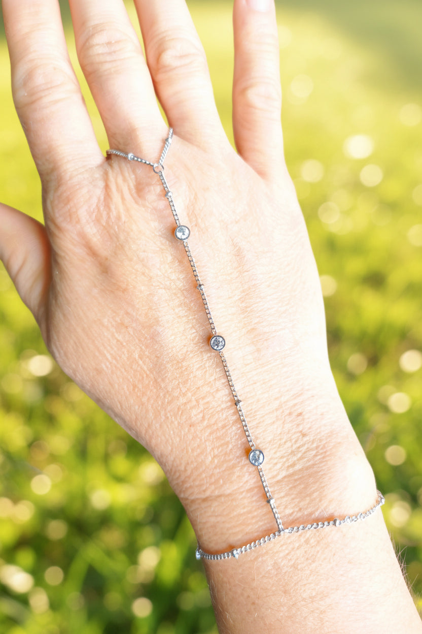 Chaîne de main en acier inoxydable argenté avec 3 zirconiums sertis le long de la chaîne et chainette de réglage, portée sur une main fond vert lumineux