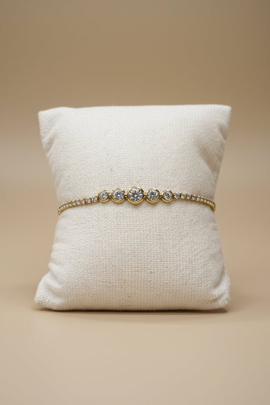 Bracelet tennis doré en acier inoxydable avec trois zircons cubiques sertis clos et chaîne pavée, présenté sur un coussin blanc - Rêve de Rose