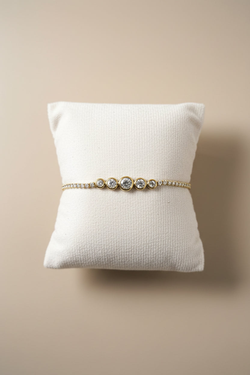 Bracelet tennis doré en acier inoxydable avec trois zircons cubiques sertis clos et chaîne pavée, présenté sur un coussin blanc - Rêve de Rose