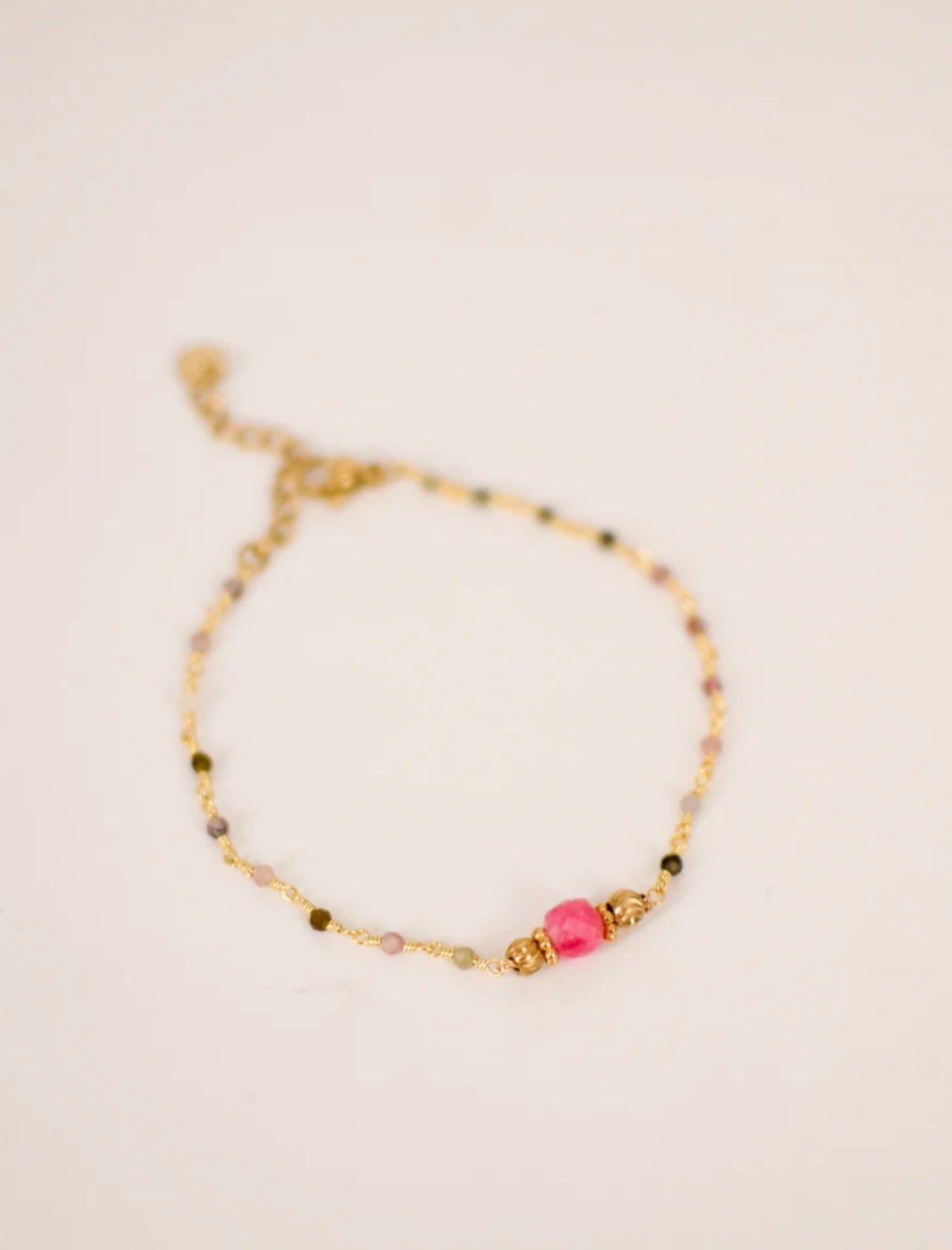 Bracelet en acier inoxydable doré composé de perles tourmaline naturelle multicolore avec pierre centrale fuchsia encadrée de perles dorées et chaînette de réglage