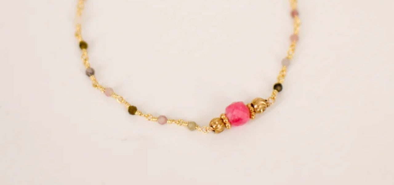 Bracelet en acier inoxydable doré composé de perles tourmaline naturelle multicolore avec pierre centrale fuchsia encadrée de perles dorées fleurées et chaînette de réglage