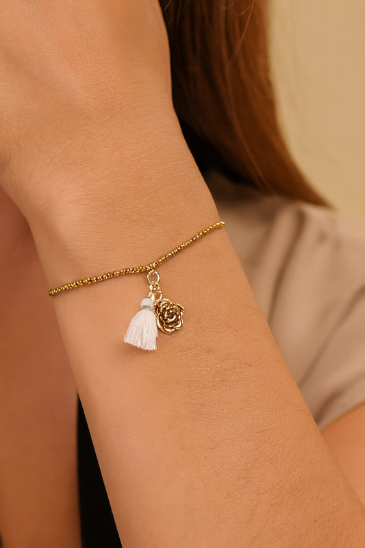 Femme portant un bracelet réglable doré avec 2 charms, une rose dorée et un pompon beige - Rêve de Rose