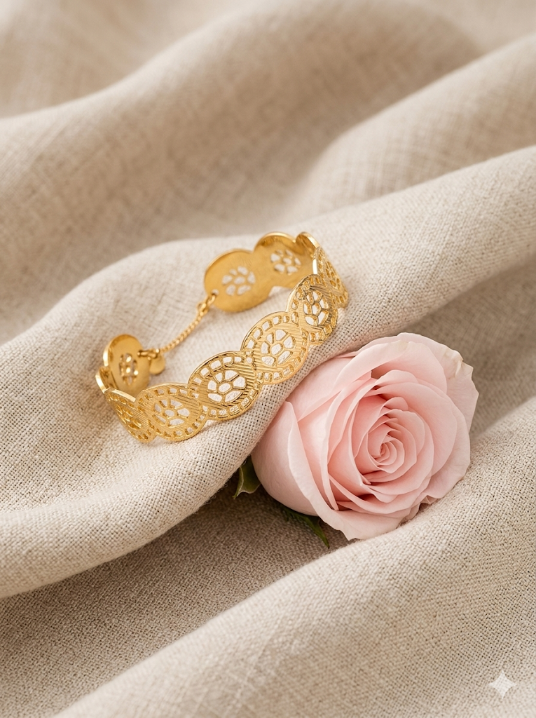 Jonc rigide ajouré en acier inoxydable doré avec motifs floraux, chaînette de sécurité et fermoir, posé sur une coquille blanche - Rêve de Rose