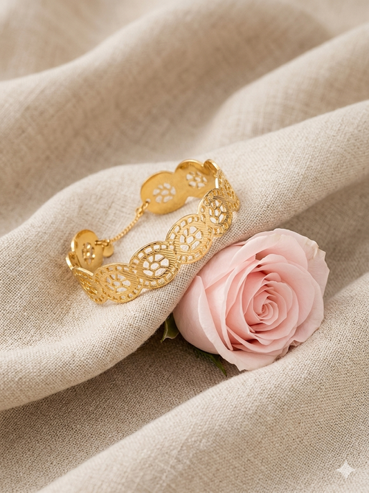 Jonc rigide ajouré en acier inoxydable doré avec motifs floraux, chaînette de sécurité et fermoir, posé sur une coquille blanche - Rêve de Rose