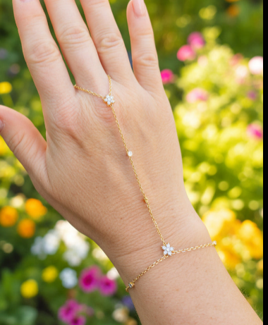 Chaîne de main dorée en acier inoxydable avec deux fleurs en zirconium et petits zirconiums le long de la chaîne, portée sur une main devant un fond floral coloré